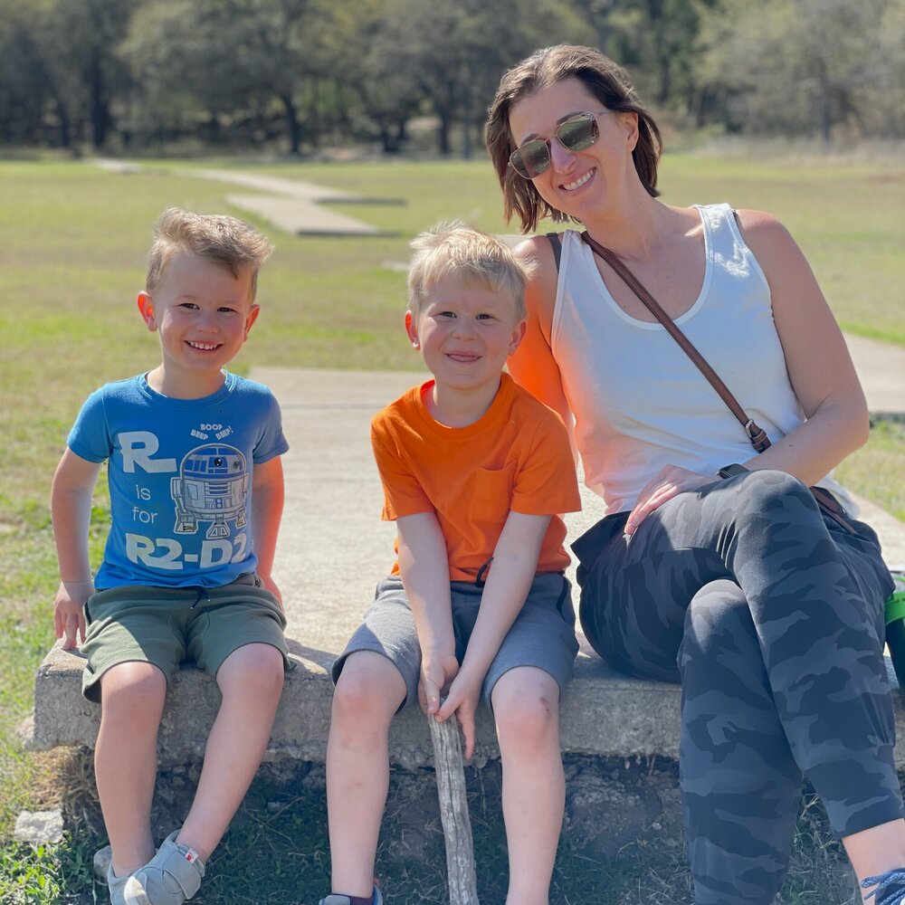 Amber and two young sons sitting on a concrete bench at a park on a sunny day.